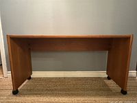 Full frontal view of mid-century modern teak console table on black casters, showing simple rectangular shape and wood grain on front panel.