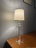 Front view of the postmodern lucite table lamp with fabric shade on wooden surface against gray wall.