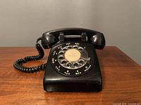 Front view of vintage rotary dial phone showing dial numbers and handset on wooden table.