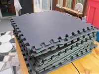 Stack of 20 black foam floor mats with interlocking edges shown stacked on a table indoors.