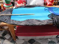 Full view of one blue mesh pool floater with black inflatable sides and head pillow, laid on a table with a measuring stick.