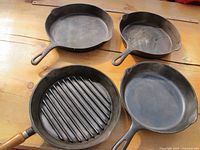 Top view showing four cast iron pans: two traditional skillets, one grill pan with wooden handle, and one skillet with spout.