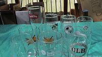 Seven assorted beer glasses with brewery logos displayed on a table.