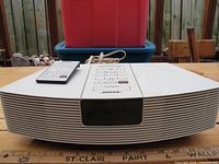 Front view of white Bose Wave Radio with remote placed on top, showing speaker grille and central control panel with digital screen.