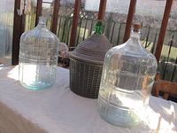 Overall view of three carboys on a table, showing two clear glass carboys and one green glass carboy inside a wicker basket.