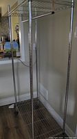 Photo of assembled clothing rack showing metal frame with poles, hanging bar and bottom shelf with no wheels attached.