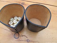 Nine dice inside two brown leather dice cups on wooden surface