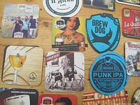 Top down view of various European beer coasters including BrewDog, Leffe, and Ježek with clear logos and colorful artwork.