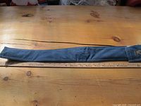 Full length of pool cue holder on a wooden table with a ruler underneath for scale.