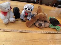 All five stuffed animals arranged in a row on a wooden table, showing variety of animals and sizes