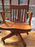 Frontal view of the wooden swivel chair showing armrests, slatted backrest, and seat splits.