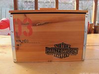 Front side of wooden cooler box showing Harley-Davidson logo, orange number 03, VIN HD1 marked and metal corner reinforcements.