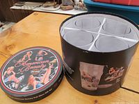 Four Harley Davidson themed pint glasses arranged in a round box, showing the packaging with pin-up girl artwork on lid.