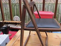 Side view showing the wooden frame, folding mechanism brass fittings, and the black cushioned seat.