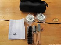 Shoe shine kit laid out on wooden table showing brushes, polish tins, and cloth