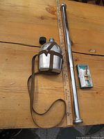 Vintage army canteen with strap beside a metal chin-up bar and a decorative bottle opener in its box on wooden table with ruler for scale