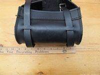 Front view of the black leather motorcycle tool pouch placed on a wooden surface with ruler showing width around 9 inches.