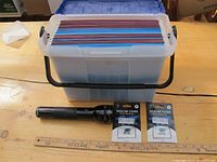 Portable file case with several colored hanging folders inside, black handle. Black Mag-Lite flashlight placed in front. Two webcam covers in packaged condition beside flashlight.