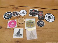 Top-down photo showing 11 beer stickers from Ontario microbreweries arranged on a wood surface including logos, text, and unique shapes.