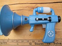 Blue Despicable Me toy shaped like a megaphone with a large speaker opening, white roller on top, and 'G' logo on the side, shown from side.
