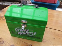 Front and top angled view of bright green metal Steam Whistle lunch box with chrome latch and handle showing the branding clearly.