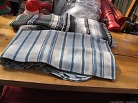 Two folded blankets visible: a light blue and white striped blanket in front, behind it a black, white, and grey striped Mexican style blanket.