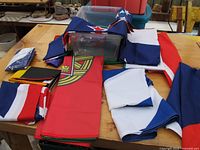 Collection of various international flags on a wooden table, folded and arranged with visible parts of different flags including the USA and New Zealand flags.