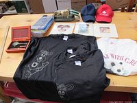 Various items including TVO t-shirts, caps, picture frames, letter desk set, oversized remote, and brass rabbit arranged on a table.