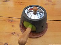 Side view of the fondue pot set on stand showing the wooden handle and stainless steel lid with wooden knob.