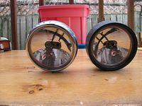 Two vintage spot lights displayed front-facing on wooden surface, showing their chrome reflective lenses.