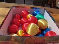 Box containing multiple round satin finish Christmas ornaments in red, gold, blue, and green colors.