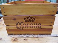 Front view of the wooden box showing the Corona logo and crown on the side with a measuring ruler in front to indicate size.