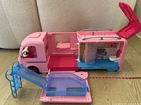 Side view of open pink Barbie camper van showing interior with bed, kitchen, blue fold-out pool with ladder, shower curtain, and toilet.