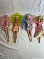 Four Barbie dolls laid out on white fabric, showing full bodies, hair, and dresses.