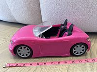 Side view showing pink convertible Barbie sports car with two seats and clear windshield next to measuring tape showing approx 6 inches long