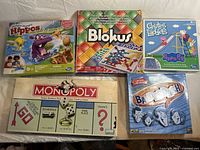 Top-down view of five board games including Monopoly, Blokus, Hungry Hungry Hippos, Balderdash, and Chutes and Ladders with Peppa Pig artwork.