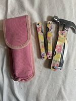 Multitool and its folded components alongside pink fabric case on white surface.
