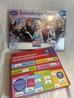 Photo showing both sealed puzzles: Disney Frozen Ravensburger 200-piece puzzle featuring characters Anna, Elsa, Olaf, Kristoff, and Sven, and a Sentence Building Puzzle with labeled colored blocks for grammar education.