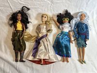Four Disney Princess dolls lying side by side in various costume styles and hair colors, showing overall condition and details