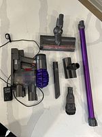 Top-down view of all components: main unit, wand, motorized brush, charger, wall mount and tools on countertop