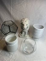 Full set of four items on beige background: lion statue, geometric glass terrarium, and two white vases with different textures