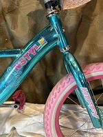 Close-up of the teal metallic frame with colorful N'Style branding, showing pink Huffy front fork and part of the tire.