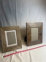 Two wooden picture frames displayed standing against a draped background, showing natural wood grain and easel backs.