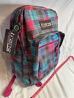 Side angle of the pink and plaid JanSport backpack showing main and front pockets, adjustable strap and tag