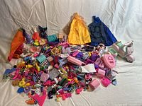 Wide view showing all fashion doll accessories spread on a white surface, including dresses, many small items, and a toy scooter.