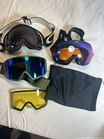 Top-down photo showing four ski goggles with different colored lenses and a black mesh bag