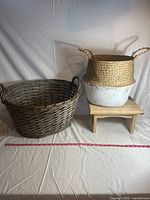 Two woven baskets and a small wooden foot stool arranged on a plain surface with measuring tape for scale.