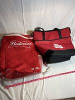 Two red zipper closure cooler bags side by side on white background, one Budweiser branded, other with 'White Lite' patch.