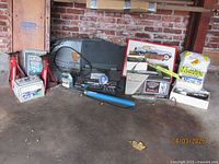 Wide view showing most automotive tools and accessories arranged on floor against brick wall. Items include jack stands, auto creeper, various pumps, towel package, socket set, diagnostic tools, and automotive prints.