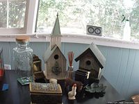 Wide view of vintage items on tabletop including glass canister, two birdhouses (church style and floral painted), pottery geese figures, tin chest, and metal leaf dish.